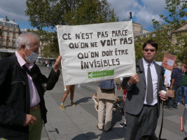 Pancarte tenue par deux personnes avec le logo de Voir Ensemble et le texte "Ce n'est pas parce qu'on ne voit pas qu'on doit être invisibles"