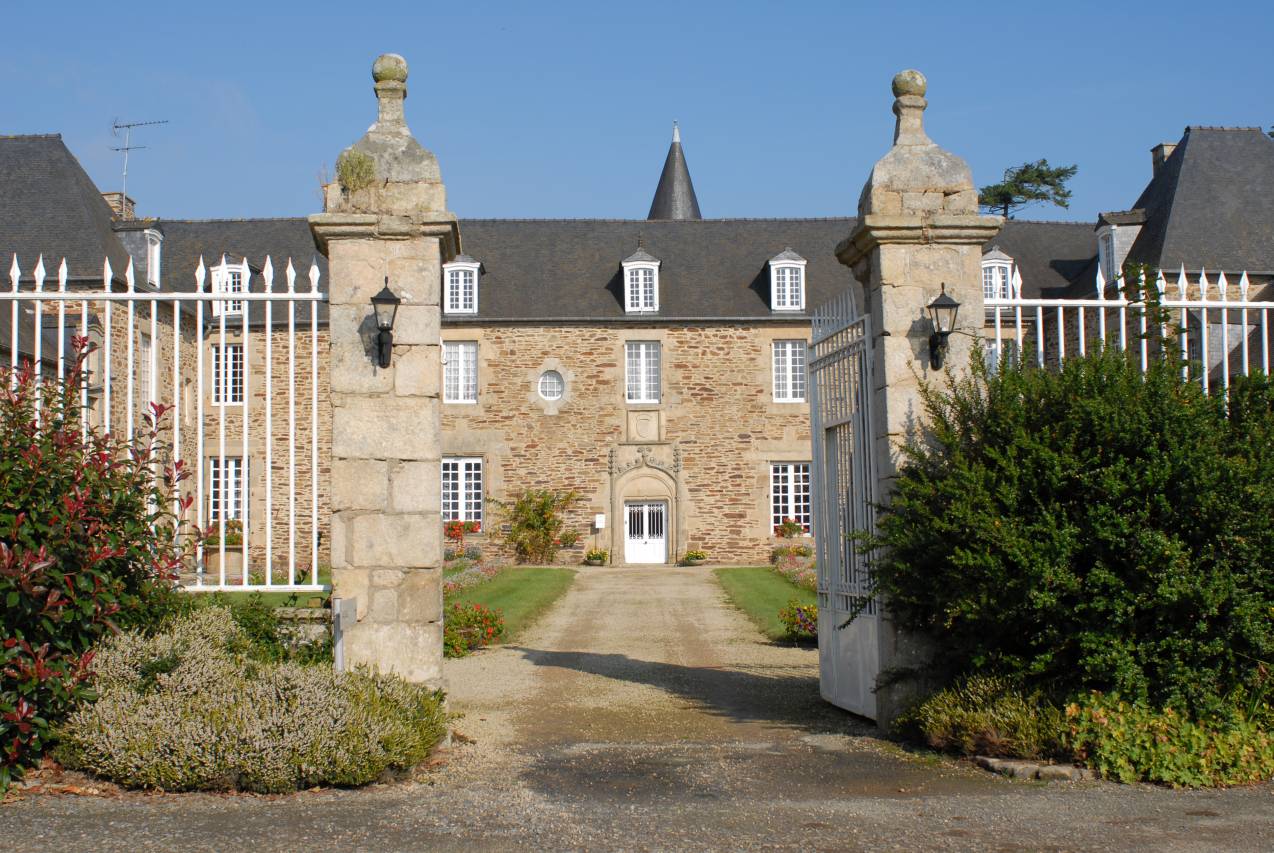 Le portail d'entrée de la Villeneuve avec vue sur le bâtiment ancien et sa porte surmontée de motifs sculptés.