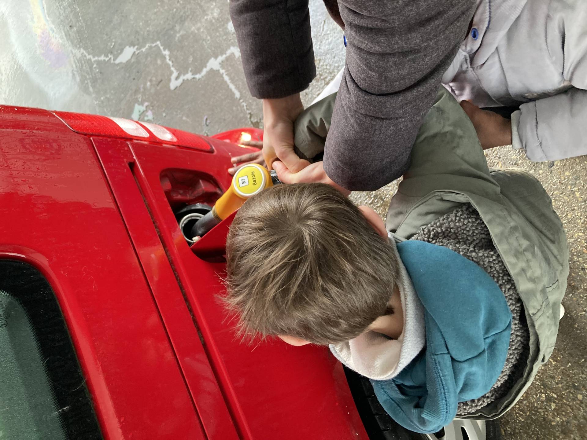 Enfant remplissant une voiture d'essence aidé par un adulte